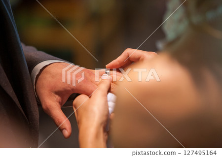Close up of loving bride and groom putting a beautiful wedding ring to the beloved partner, marry me 127495164
