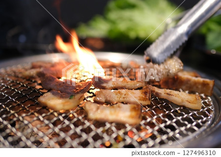 Grilling meat flames Man grilling burgers, sausages, and vegetables on a charcoal kettle grill during golden hour. Perfect for summer BBQ, outdoor cooking, and food themes 127496310