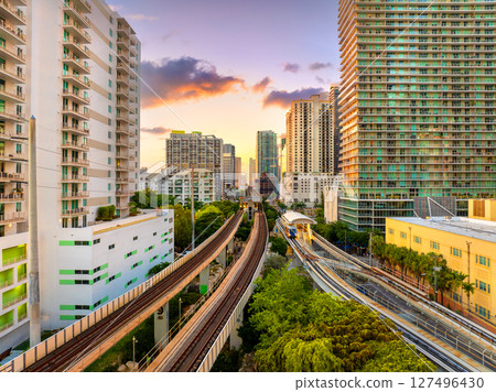 Railroad tracks and public train line run through the heart of Miami Brickell downtown in Florida, USA, surrounded by sunset lit skyscrapers of the financial district 127496430