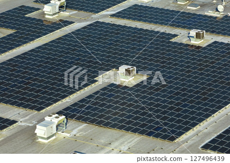 Production of sustainable energy. Aerial view of solar power plant with blue photovoltaic panels mounted on industrial building roof for producing green ecological electricity 127496439