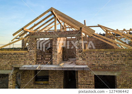 Private residential house with wooden roof frame structure under construction. Unfinished brick building under development. 127496442