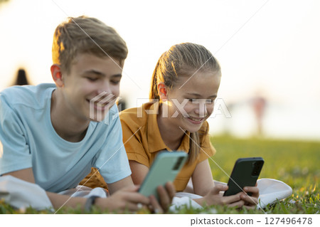 Positive children messaging on their mobile phones with friends outdoors in summer park. Positive children messaging on their mobile phones with friends outdoors in summer park. 127496478