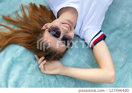 Portrait of young teenage girl in sunglasses laying down on blue cloth background. 127496480