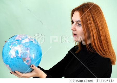 Portrait of a sad worried young woman holding geographic globe of the world in her hands. Travel destination and planet protection concept. 127496512