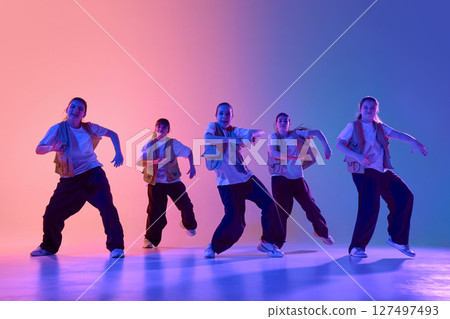 Energetic dance group performing under vibrant colorful lighting in urban dance studio 127497493