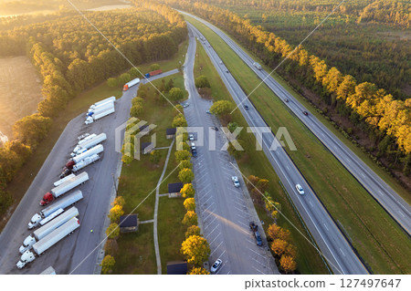 Large truck stop with resting area near busy American interstate freeway. Parking place during big rig interstate travel Large truck stop with resting area near busy American interstate freeway. Parking place during big rig interstate travel 127497647