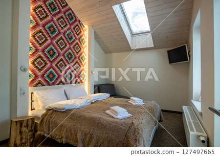 Interior of a spacious hotel bedroom on attic floor with fresh linen on a big double bed. Cozy contemporary mansard room in a modern house. 127497665