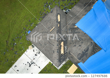 Hurricane Ian damaged house rooftop covered with protective plastic tarp against rain water leaking until replacement of asphalt shingles. Aftermath of natural disaster Hurricane Ian damaged house rooftop covered with protective plastic tarp against rain water leaking until replacement of asphalt shingles. Aftermath of natural disaster 127497686