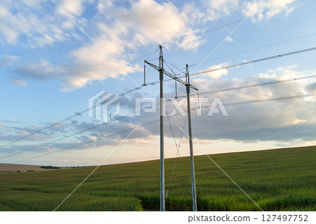 High voltage tower with electric power lines between green agricultural fields. Transfer of electricity concept. 127497752