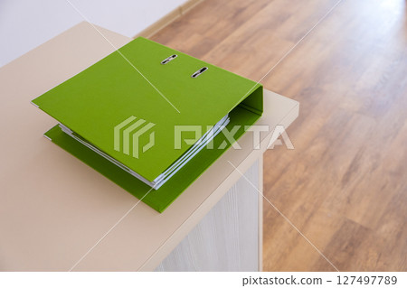 Green binder with office documents on a working table. 127497789