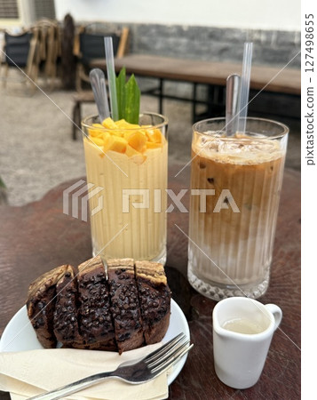 vertical photo banana bread two drinks iced latte Delicious mango float cake in glasses on wooden board. Filipino sweet cuisine 127498655