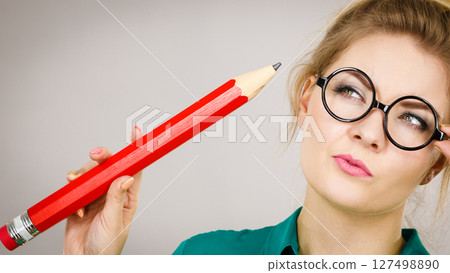 Woman confused thinking, big pencil in hand Woman confused thinking, big pencil in hand 127498890