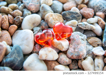 Two glass red bright heart on other stones near the river with sun weather. Two glass red bright heart on other stones near the river with sun weather. 127499154
