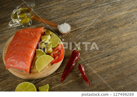 Meat red salmon fish, tomatoes, spices, lemon, green olives and olive oil on wooden kitchen table. 127499289