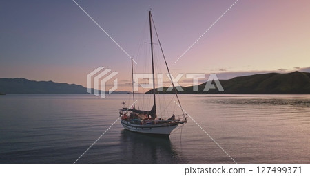 Romantic purple hues sky during sunset, casting a serene glow over calm sea waters. An anchored sailboat rests peacefully, distant islands creating an idyllic escape. Amazing nature travel background Romantic purple hues sky during sunset, casting a serene glow over calm sea waters. An anchored sailboat rests peacefully, distant islands creating an idyllic escape. Amazing nature travel background 127499371