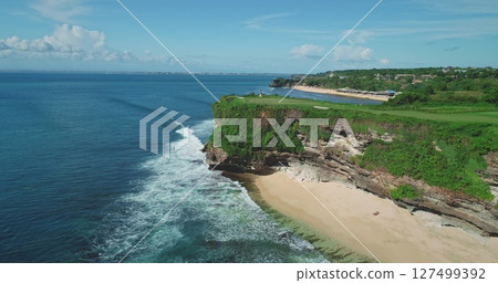 Stunning aerial view of Pantai Dreamland Beach in Bali, Indonesia, featuring turquoise waters, white sands, lush cliffs, and crashing waves in a tropical paradise 127499392