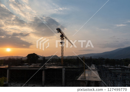 Construction site with cranes against the background of the evening sky and the sun. Construction site with cranes against the background of the evening sky and the sun. 127499770