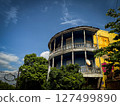 Rustic Georgian balcony house with curved wooden facade and satellite dish, framed by vibrant greenery and dramatic sky in an old historic neighborhood 127499890