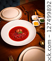 Traditional Ukrainian borscht with beef and dill served in a white bowl, styled with condiments and pastry on a warm wooden restaurant table 127499892
