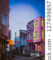 Colorful Turkish street with vivid facades, flags, and outdoor signs, captured under bright daylight with local people and cars in a lively neighborhood scene 127499897