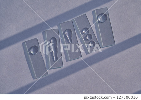 The texture of serum or micellar water on slides on a blue background with streaks of shadows. The texture of serum or micellar water on slides on a blue background with streaks of shadows. 127500010