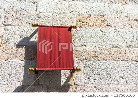 Red banner on stone wall in sunlight. Minimalist composition, urban decor, and Mediterranean architectural texture. Copy space 127500160