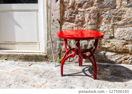 Bright red stool beside stone wall. Street furniture, color contrast, and outdoor simplicity. Bright red stool beside stone wall. Street furniture, color contrast, and outdoor simplicity. 127500193