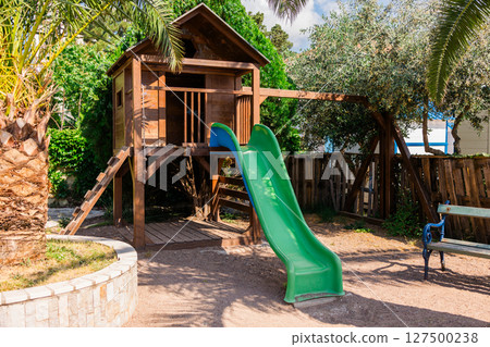 Wooden playground with treehouse and slide in a sunny garden. Outdoor fun, nature play, and childhood adventure concept. 127500238