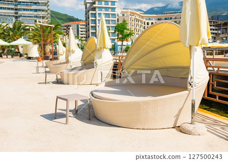 Modern canopy sunbeds on resort pier under bright summer light. Outdoor leisure, premium comfort, and waterfront tourism Modern canopy sunbeds on resort pier under bright summer light. Outdoor leisure, premium comfort, and waterfront tourism 127500243