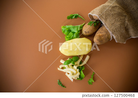 Root vegetable in a sack and sliced potatoes on a brown background Root vegetable in a sack and sliced potatoes on a brown background 127500468