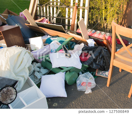 Waste in a city near the house. Big garbage with old wood furniture, toys, boxes, plastic bags on a street and green grass in spring sunny trash dump day in Germany.  127500849