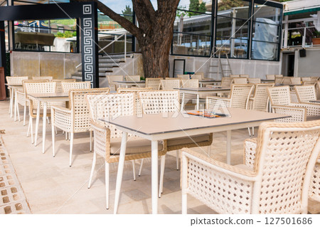 Modern restaurant terrace with set tables and chairs. Casual dining, cozy atmosphere, and summer hospitality experience. Modern restaurant terrace with set tables and chairs. Casual dining, cozy atmosphere, and summer hospitality experience. 127501686