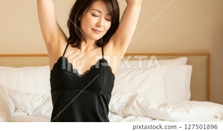 A Japanese woman in a black camisole stretching on the bed 127501896