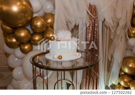 Elegant White Cake with Gold Accents for Birthday Celebration Backdrop with Balloons and Feathers Elegant White Cake with Gold Accents for Birthday Celebration Backdrop with Balloons and Feathers 127502262