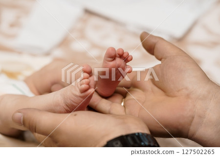 Tender Moment: Dad Holding Baby's Foot in Hand - New Parenthood, Love, Connection, Soft Colors, Family Theme, Beige Background Tender Moment: Dad Holding Baby's Foot in Hand - New Parenthood, Love, Connection, Soft Colors, Family Theme, Beige Background 127502265