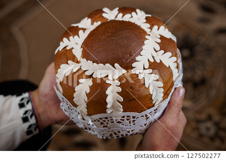 Traditional Ukrainian Easter Bread Paska Held in Hands with Lace Detail, Brown Crust, Cultural Celebration, Rich Texture, Warm Lighting. 127502277