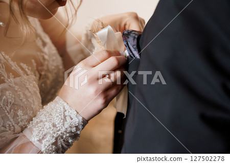 Romantic Wedding Boutonniere Placement: Bride Pinning Floral Corsage to Groom's Lapel, Intimate Moment, Black Suit, Pearl Detail. 127502278