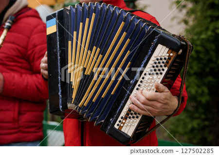 Blue Accordion Player Performing Outdoors: Cultural Music Event, Traditional Instrument, Red Jacket, Folk Style, Artistic Photography, Bright Daylight 127502285