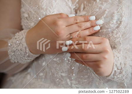 Bridal Hands Showcase Sparkling Diamond Engagement Ring on White Wedding Dress, Close-up Detail of Love and Commitment Gesture 127502289
