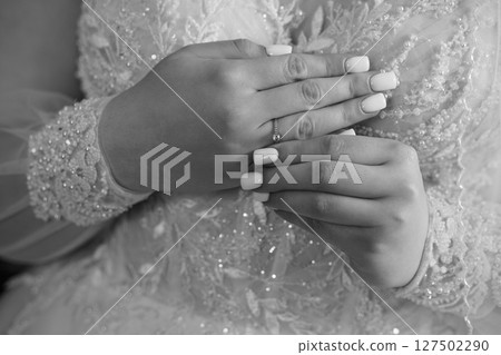 Elegant Wedding Ring Close-Up: Bride's Hands Displaying Diamond Band on Lace Dress, Black and White Photography. 127502290