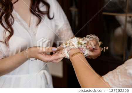 Wedding Preparation Corsage Application: Bride Getting Wrist Flower Detail Assistance, White Lace Robes, Tender Moment, Soft Lighting Wedding Preparation Corsage Application: Bride Getting Wrist Flower Detail Assistance, White Lace Robes, Tender Moment, Soft Lighting 127502296