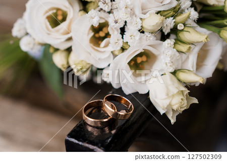 Wedding Rings and White Roses Bouquet on Dark Wood, Elegant Bridal Symbolism, Romantic Ceremony, Gold, Ivory, Floral Arrangement, Close-Up, Texture Wedding Rings and White Roses Bouquet on Dark Wood, Elegant Bridal Symbolism, Romantic Ceremony, Gold, Ivory, Floral Arrangement, Close-Up, Texture 127502309