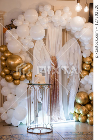 Elegant White and Gold Balloon Arch Backdrop with Cake Table for Celebrations, Parties, Weddings, Luxury Events, and Angel Wings Theme Elegant White and Gold Balloon Arch Backdrop with Cake Table for Celebrations, Parties, Weddings, Luxury Events, and Angel Wings Theme 127502320