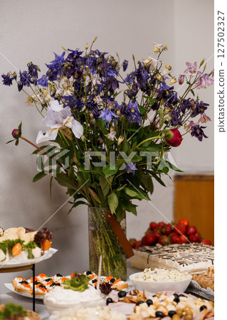 Beautiful Banquet Table Setting with Blue Flowers, Desserts and Fresh Fruit: Elegant Food Display with Lilies and Festive Treats 127502327