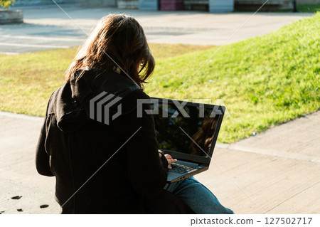 Young woman working on laptop sitting in public park Young woman working on laptop sitting in public park 127502717