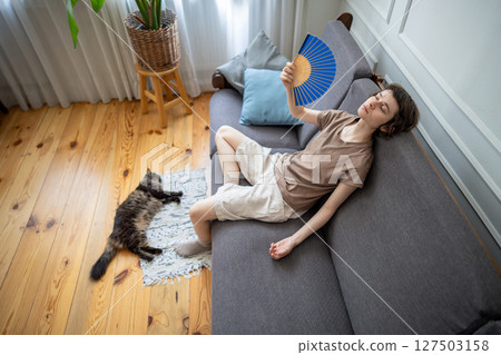 Suffering woman fanning, enduring high temperatures with pet struggling in airless apartment in heat Suffering woman fanning, enduring high temperatures with pet struggling in airless apartment in heat 127503158