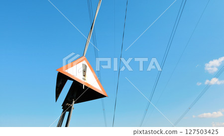 Red triangle with exclamation mark on steel cable of electric pylon, clear sky in background 127503425
