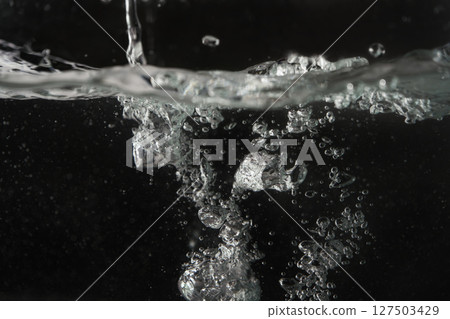 Water splashing as it's poured into aquarium tank, black background 127503429