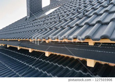 Closeup of house roof top covered with ceramic shingles. Tiled covering of building under construction 127503906