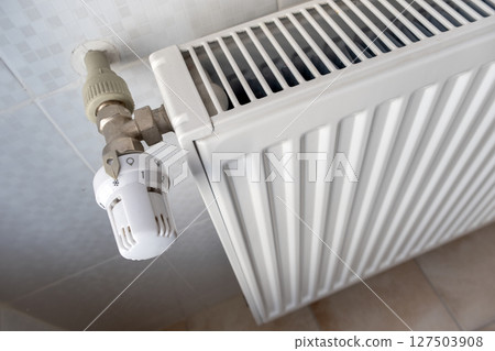 Closeup of heating radiator valve for comfortable temperature regulation on metal radiator on inrerior wall. 127503908